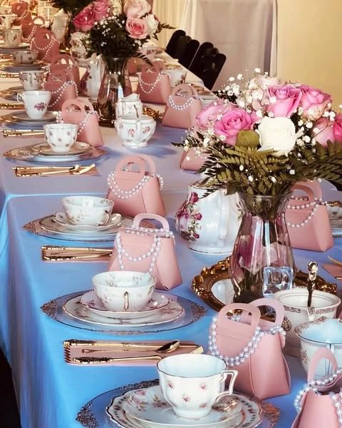 An elegant table setting featuring floral china, rose centerpieces, and pink purse-shaped party favors.