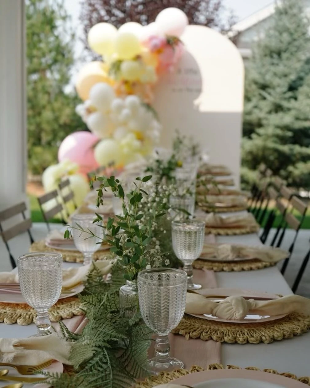 A boho baby shower place setting features a woven placemat and greenery centerpiece.