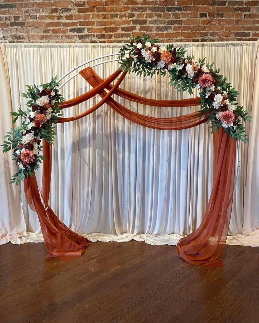 Circular arch decorated with rust-colored fabric and flowers for a party photo backdrop.