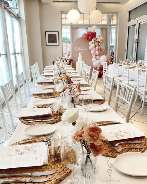 Long white dining table set for a wildflower baby shower with woven placemats and bud vase centerpieces.