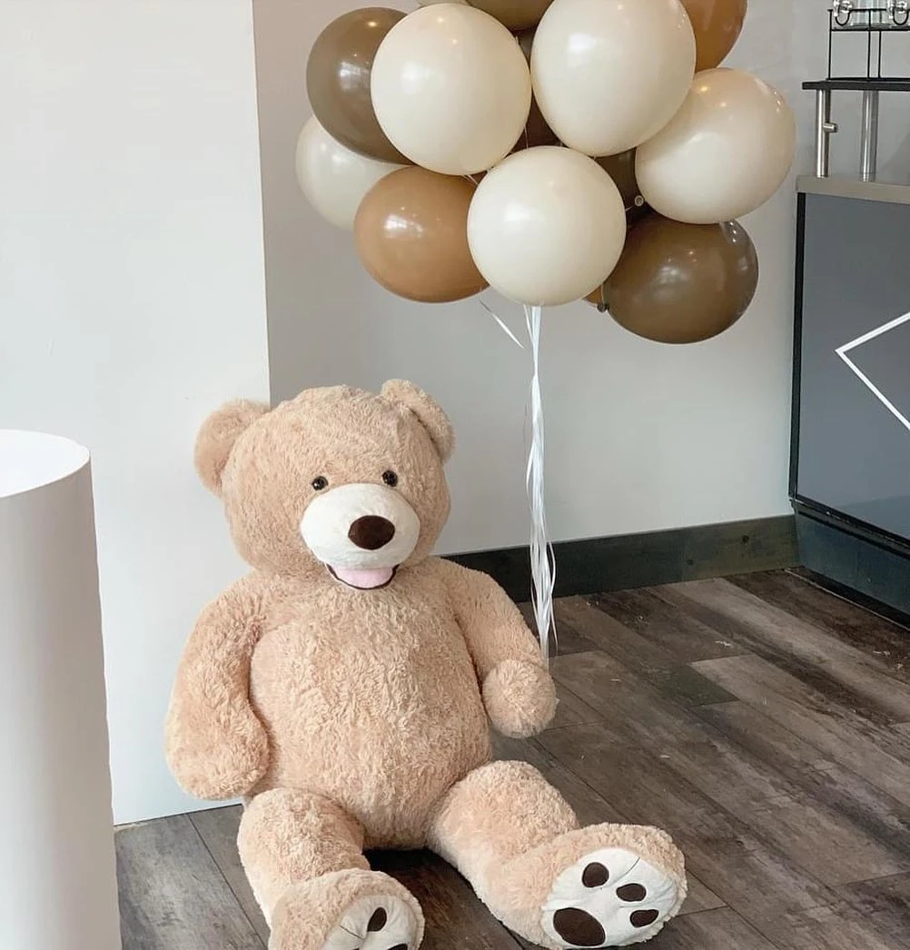 Large teddy bear with neutral balloons as floor decor for a baby shower.