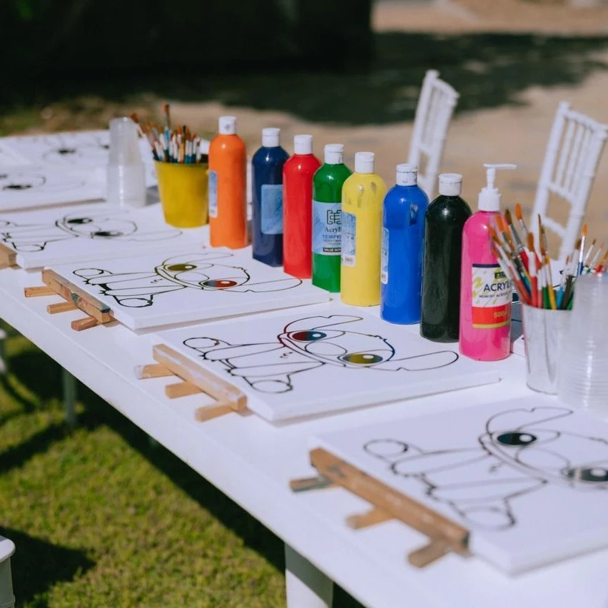A party setup for a Stitch painting activity with pre-drawn canvases, mini easels, and colorful paints on a table.