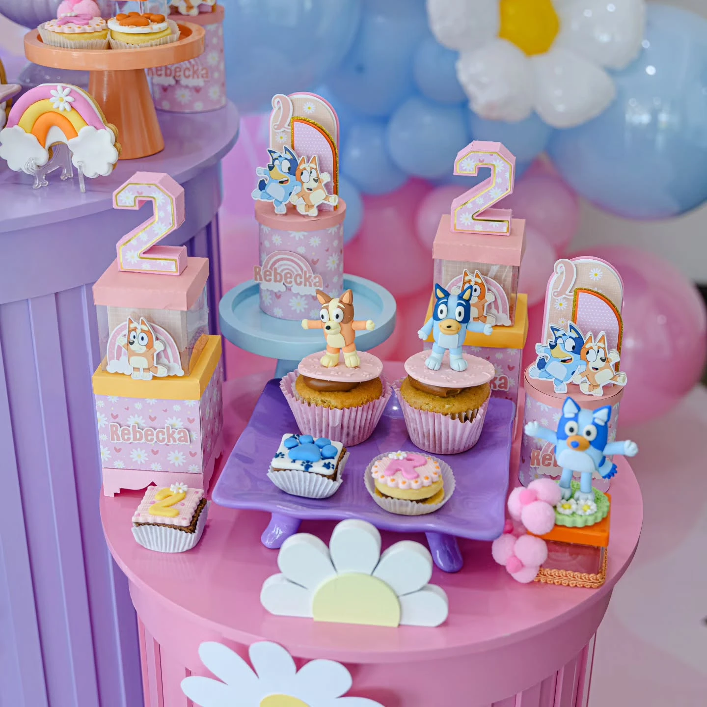 A Bluey-themed dessert table with cupcakes, cookies, and treat boxes in pastel colors.