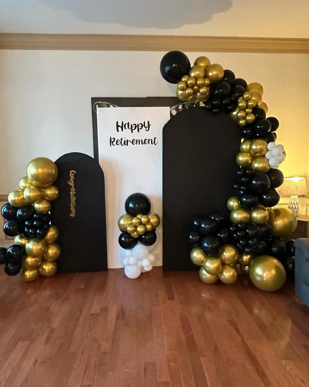 A retirement party photo backdrop with black and gold panels and a large balloon arch.