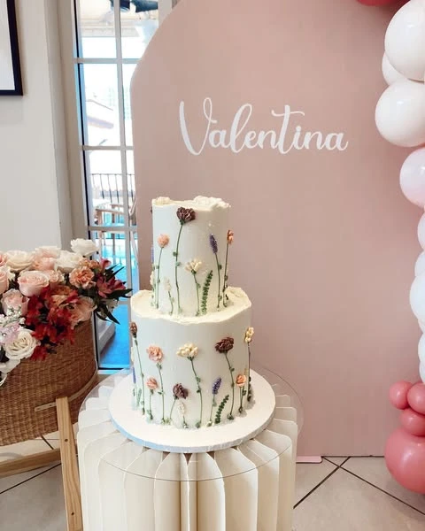 Two-tier white cake with piped buttercream wildflowers for a baby shower.