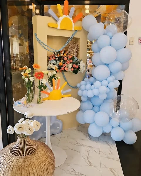 A welcome table at a baby shower decorated with a small sun cutout and a light blue balloon garland.