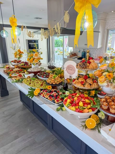 A long kitchen island covered in a baby shower brunch buffet with pastries, salads, and fruit.