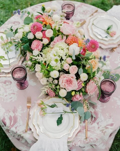 A spring bridal shower tablescape with a large pink floral centerpiece and purple glassware.