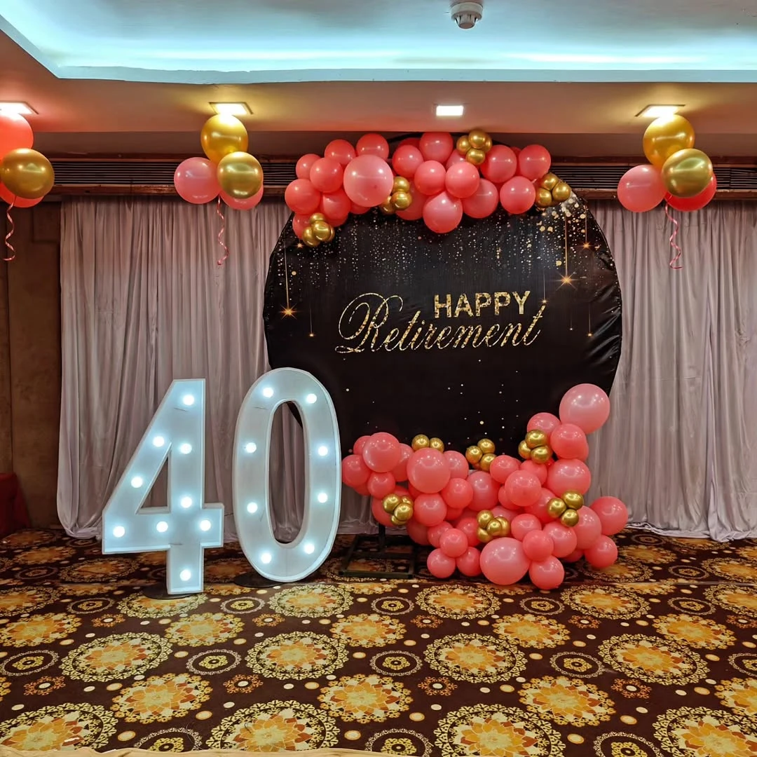 An elegant retirement party photo backdrop with gold script and a pink and gold balloon arch.