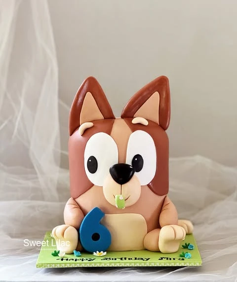 A sculpted birthday cake shaped like a Bluey character holding a blue number six.
