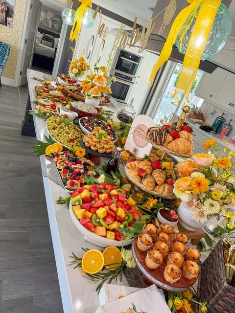 An angled view of a brunch buffet on a kitchen island, highlighting tiered stands with muffins and croissants.