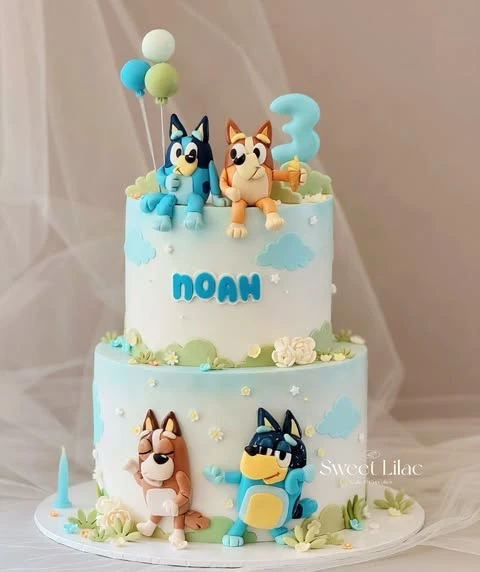 A two-tiered Bluey birthday cake with fondant figures of Bluey, Bingo, Bandit, and Chilli.
