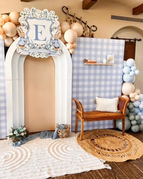 Peter Rabbit baby shower photo backdrop with a gingham wall, white arch, and wooden bench.