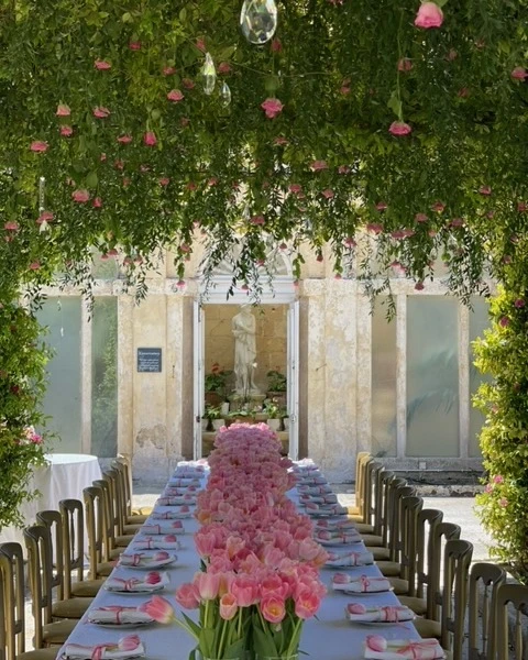 Long dining table for a spring bridal shower with a dense pink tulip runner and a hanging green canopy with pink flowers.