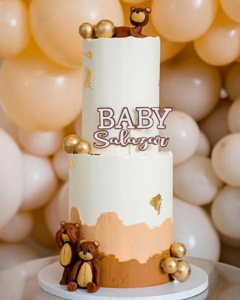 A two-tier 'We Can Barely Wait' baby shower cake with fondant teddy bears and gold details.