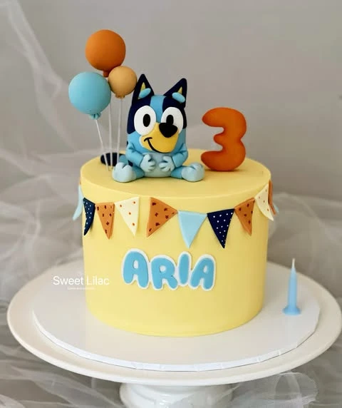 A yellow single-tier Bluey birthday cake with a Bluey figurine and a small pennant banner.