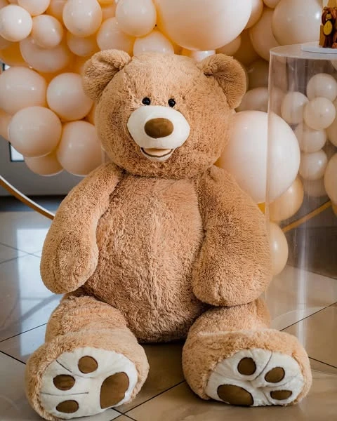 A large, light-brown teddy bear prop sitting on the floor as part of baby shower decorations.