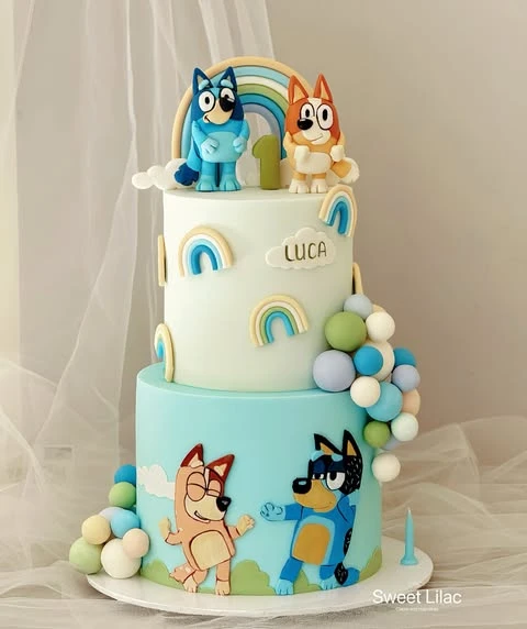 A two-tiered Bluey birthday cake decorated with rainbows and a cascade of colorful fondant balls.