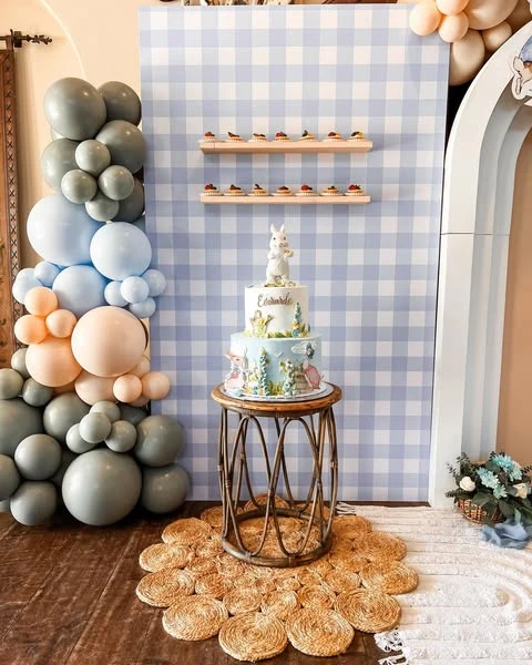 Peter Rabbit themed cake on a rattan stand against a gingham backdrop with balloons.