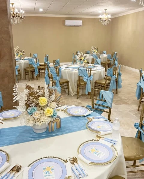 An event hall with multiple round tables decorated in a cohesive blue, yellow, and gold 'Here Comes the Sun' baby shower theme.