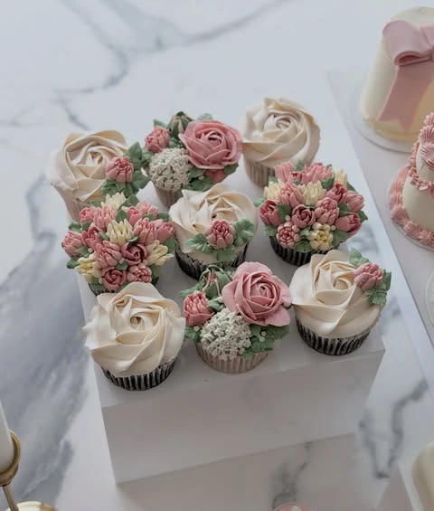 Detailed view of floral-frosted cupcakes grouped together on a low white display riser for a baby shower.