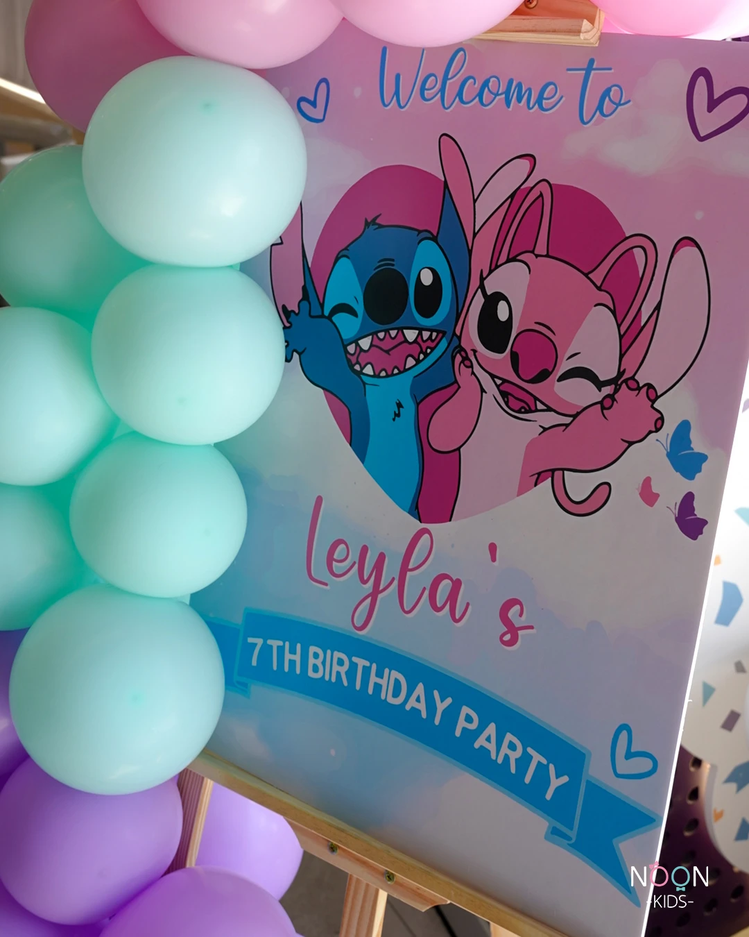 A welcome sign for a Stitch and Angel birthday party on an easel, framed by balloons.