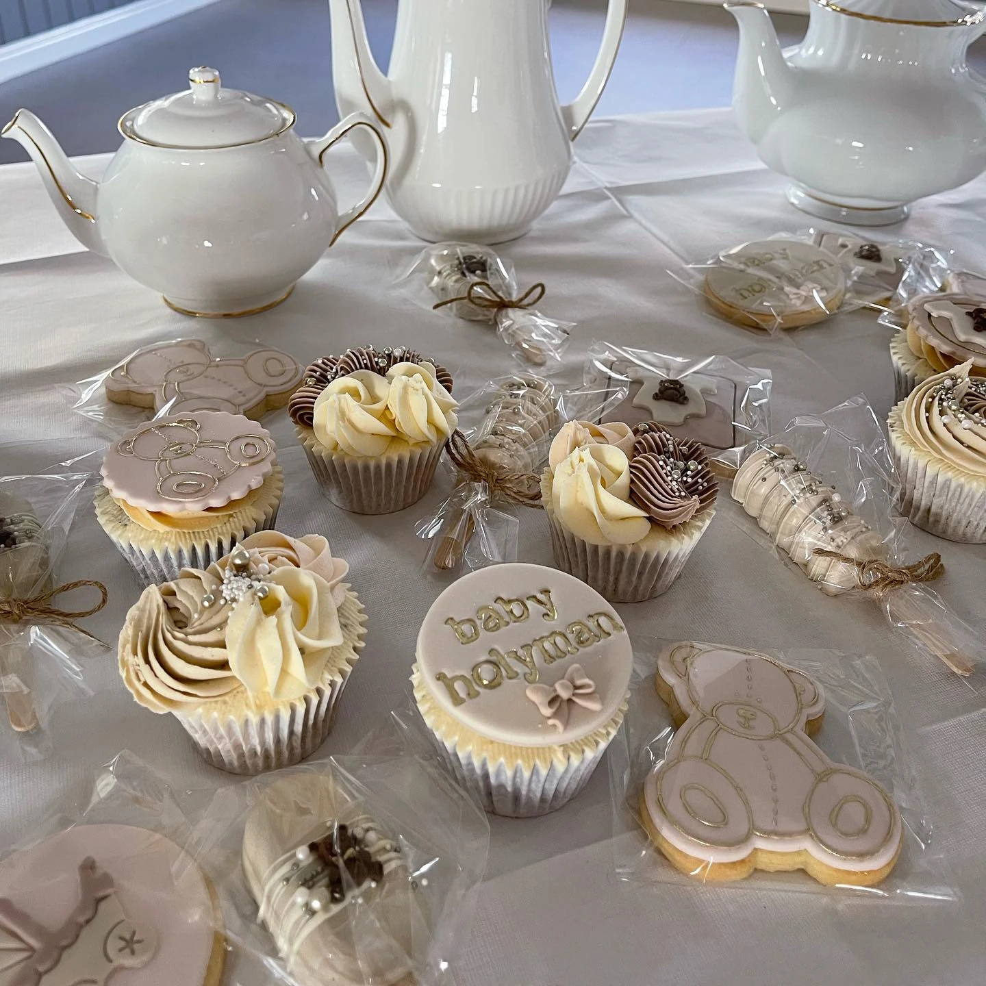 A display of 'we can barely wait' themed desserts, including teddy bear cookies and cupcakes in neutral colors.