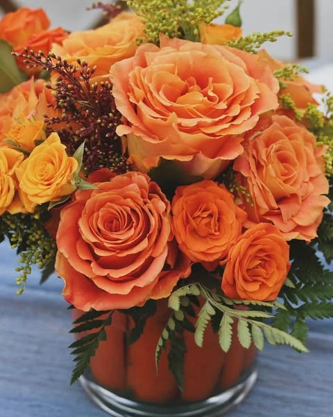of a floral centerpiece with orange roses in a glass vase lined with whole carrots.