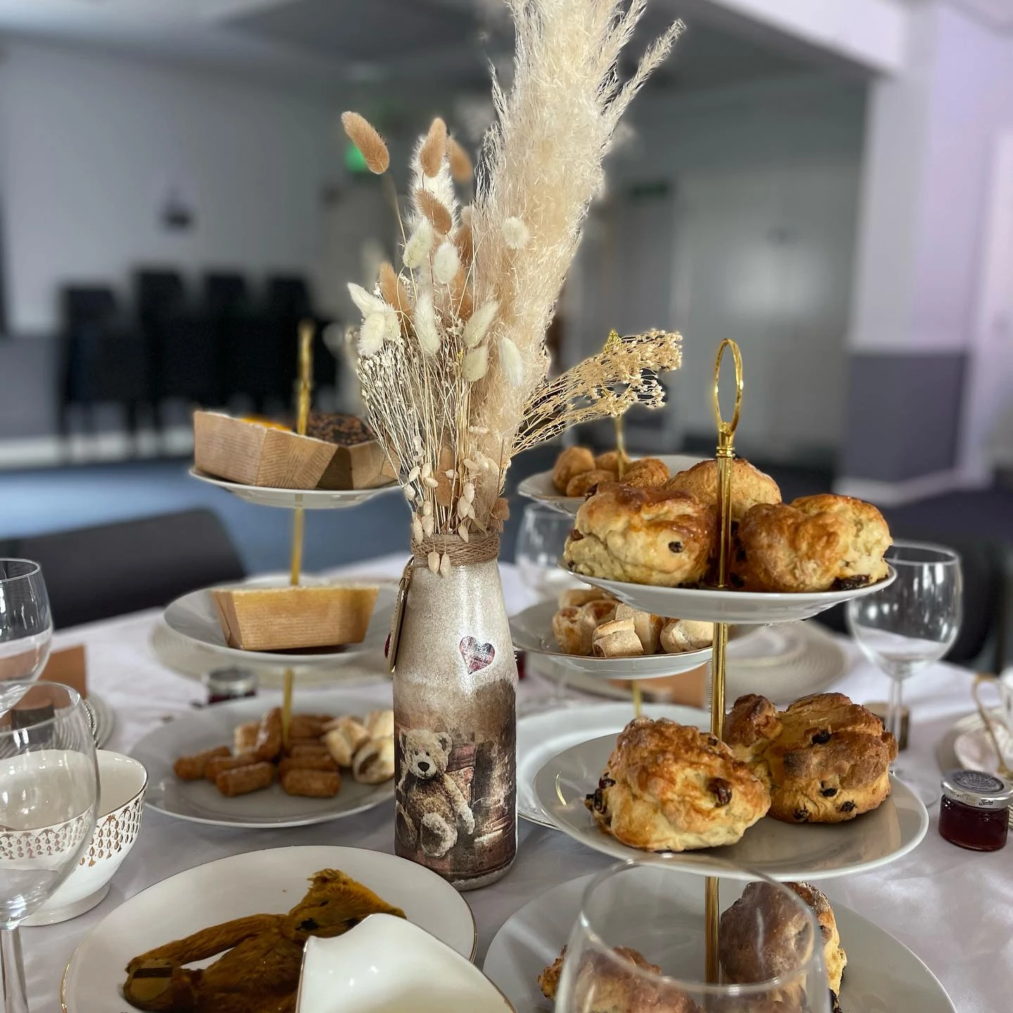 Baby shower table setting with a teddy bear vase centerpiece filled with pampas grass.