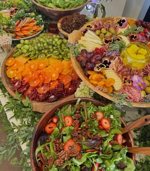 A charcuterie board with edible pansies and a colorful fruit platter on a baby shower food table.