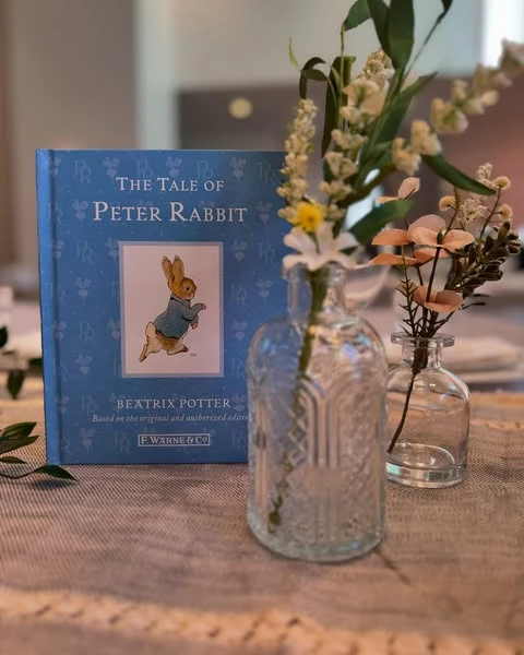 A copy of 'The Tale of Peter Rabbit' used as a baby shower centerpiece next to a bud vase.