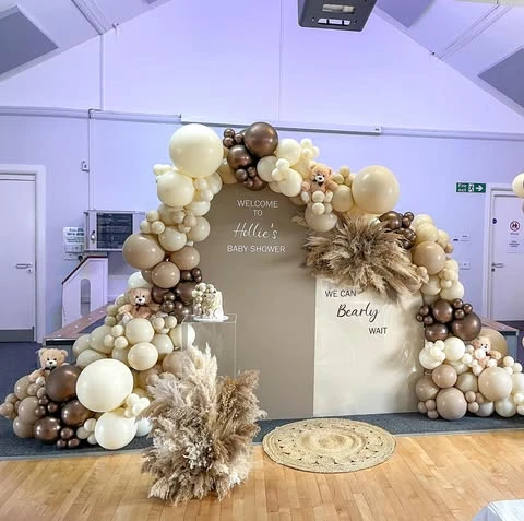 Wide view of a 'we can barely wait' baby shower backdrop with a large neutral balloon arch and teddy bears.