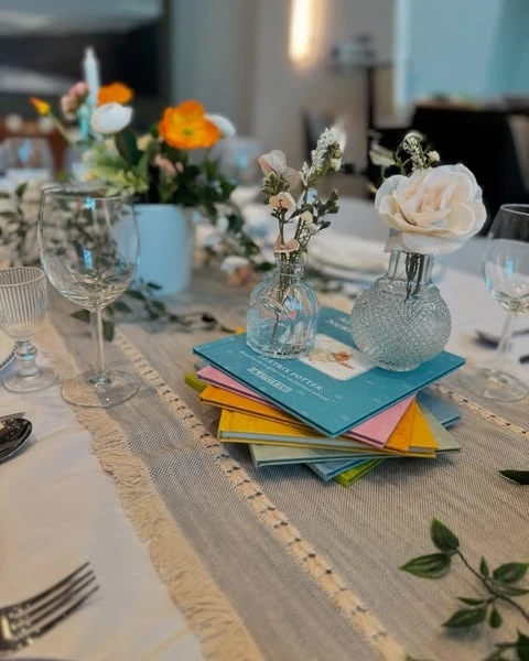 A stack of colorful Beatrix Potter books used as a centerpiece riser for flowers at a baby shower.
