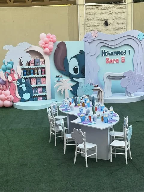 Elaborate Stitch-themed birthday party setup with a large Stitch cutout, layered backdrops, and a custom-shaped kids' table.