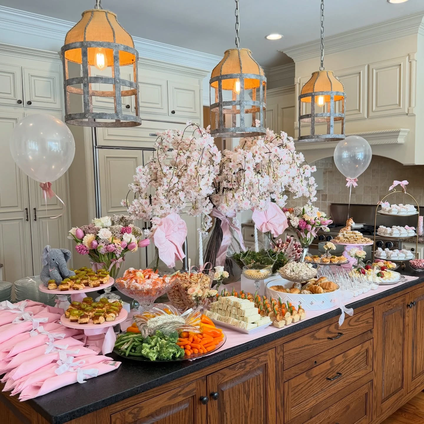 A long kitchen island set up as a baby shower food table with a variety of appetizers, desserts, and pink decorations.