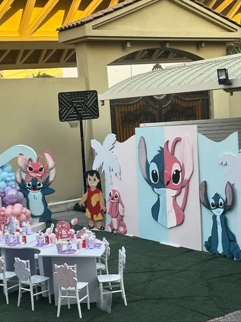 Outdoor Stitch party decor featuring life-sized cutouts of Lilo, Stitch, and Angel next to a themed backdrop wall.