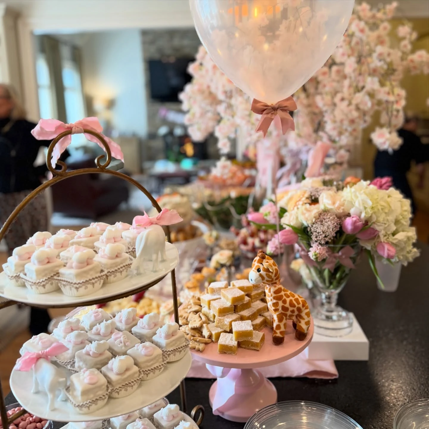 A baby shower dessert display with a tiered stand of petit fours and a pink stand with lemon bars.