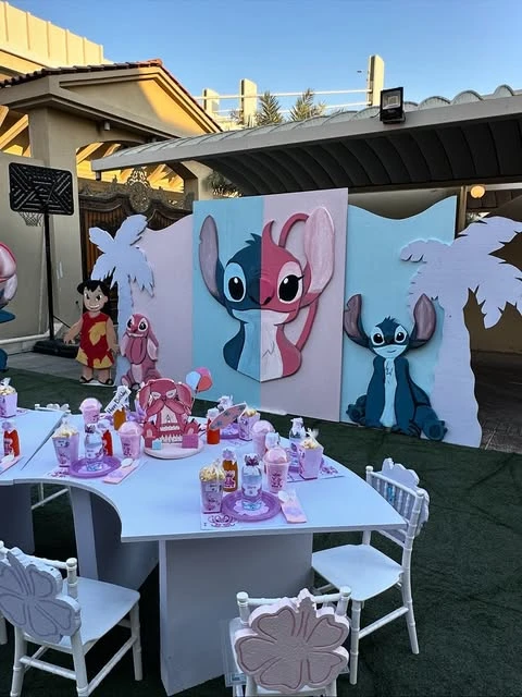 Stitch-themed party table with custom cups, popcorn boxes, and chairs decorated with pink hibiscus flowers.
