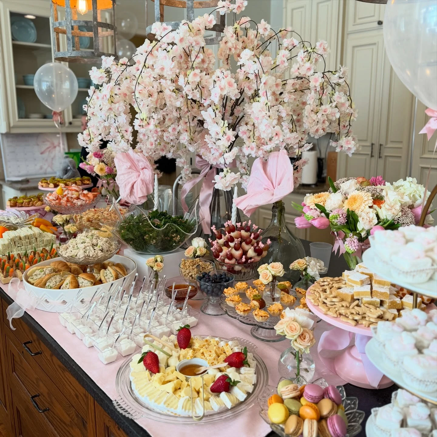 An overhead view of a baby shower food table showing a cheese plate, macarons, fruit skewers, and other appetizers.