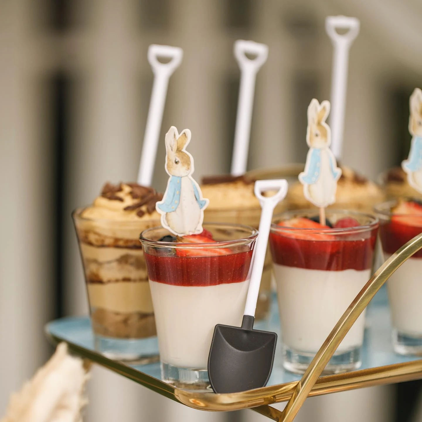 Individual desserts in glass cups, topped with Peter Rabbit cutouts and served with miniature shovel spoons.