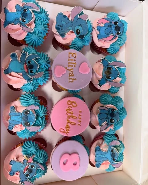 A box of Stitch-themed cupcakes with pink and blue frosting and personalized fondant toppers.