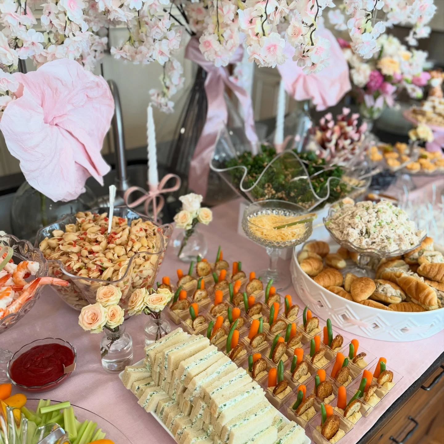 Baby shower food including finger sandwiches, pasta salad, and individual vegetable cups.