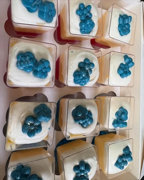 Individual dessert cups with a white topping and blue floral decorations, matching a party theme.