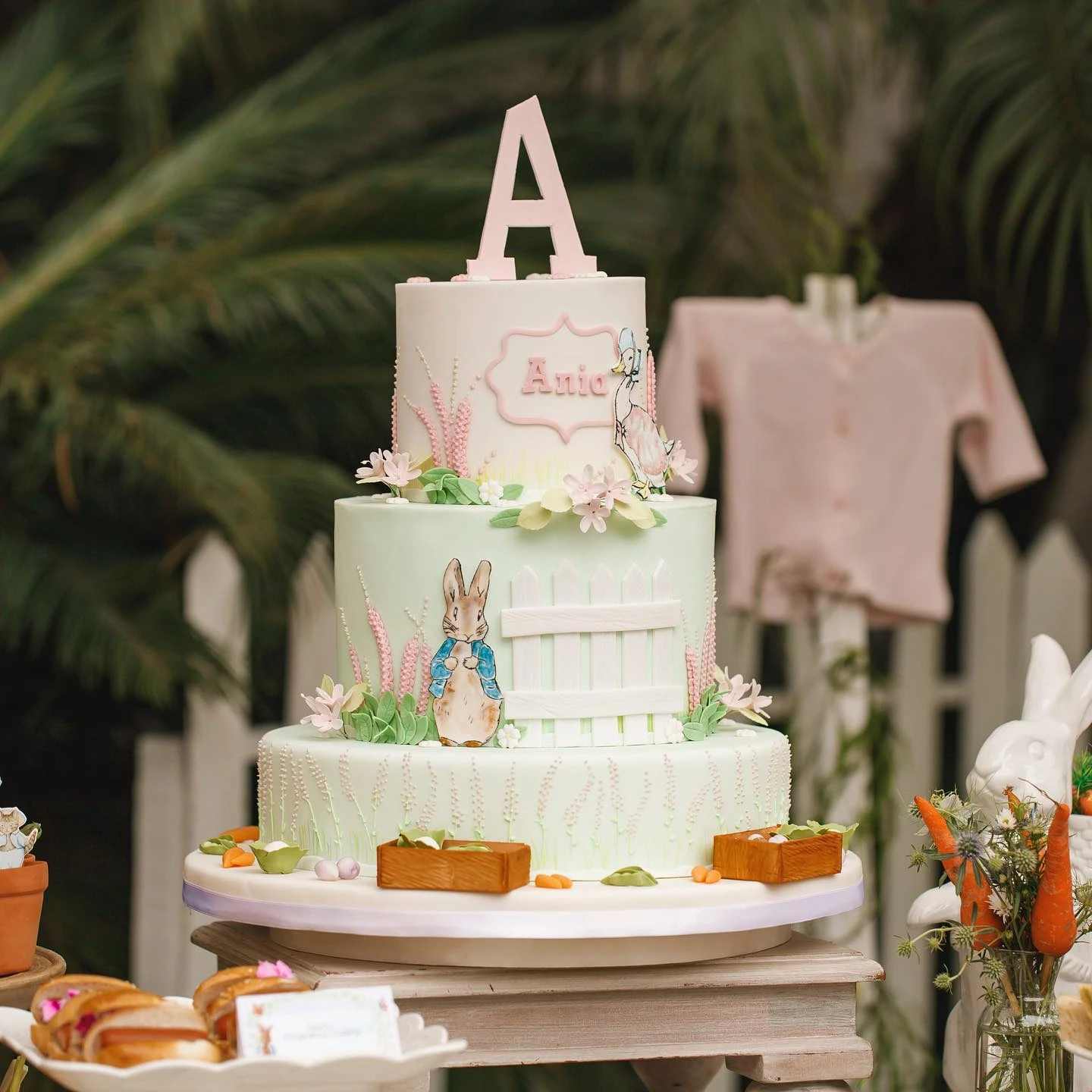 A three-tiered Peter Rabbit cake with a fondant picket fence detail on the middle layer.