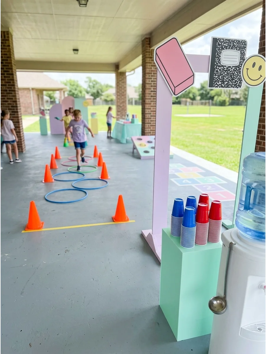 An outdoor field day setup with orange cones and blue hula hoops on green grass.