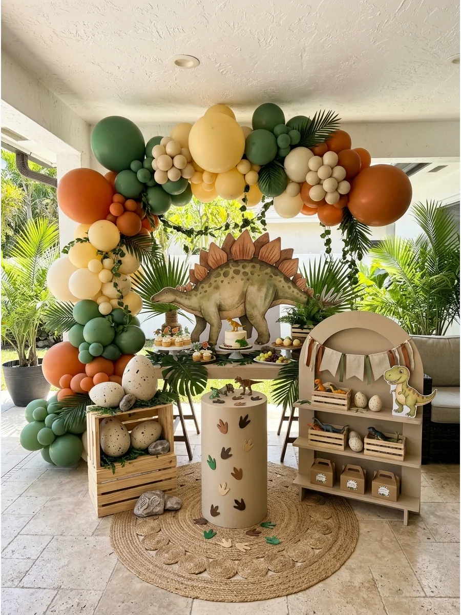 A dinosaur themed birthday party with green and orange balloons and a large dinosaur cutout.