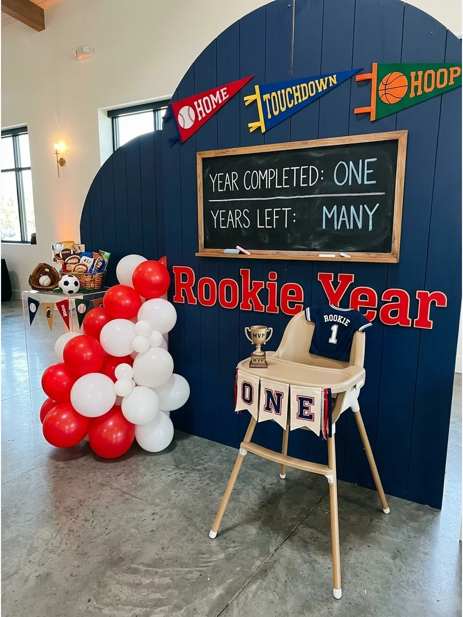 A rookie year sports theme with a scoreboard backdrop and red balloons.