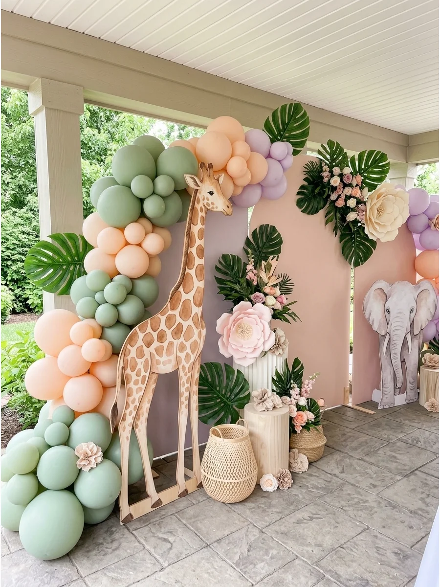A safari birthday setup with sage balloons and a wooden giraffe.