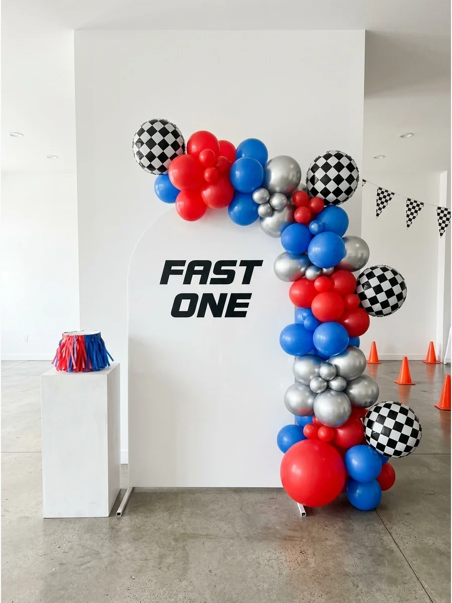 A bold red and black balloon arch with checkered accents around a birthday sign.
