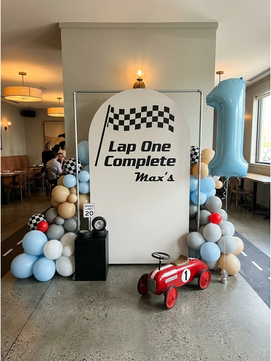 A finish line backdrop for a first birthday with a red ride-on car prop.